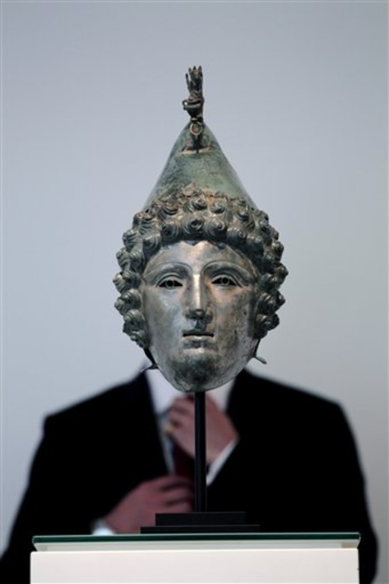 A Christie's employee poses for photographs behind a Roman bronze helmet found with the use of a metal detector, at the auction house's offices in London, Monday, Sept. 13, 2010.